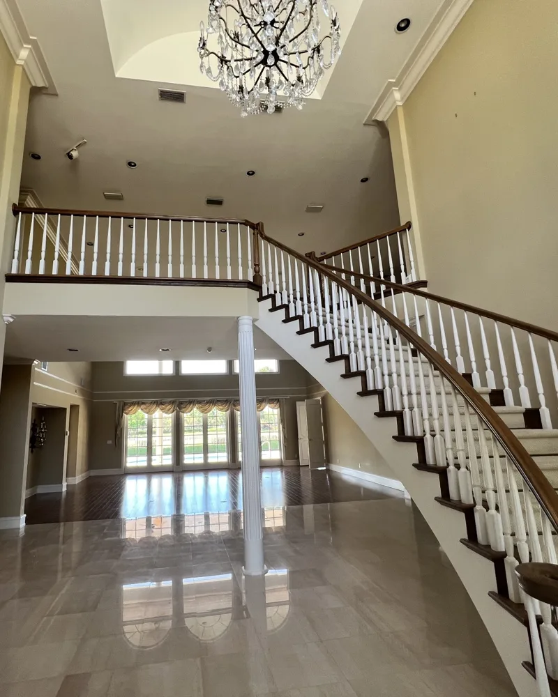 Before: two-story foyer with tan walls, wallpaper, marble floor and a curved staircase with stained handrails