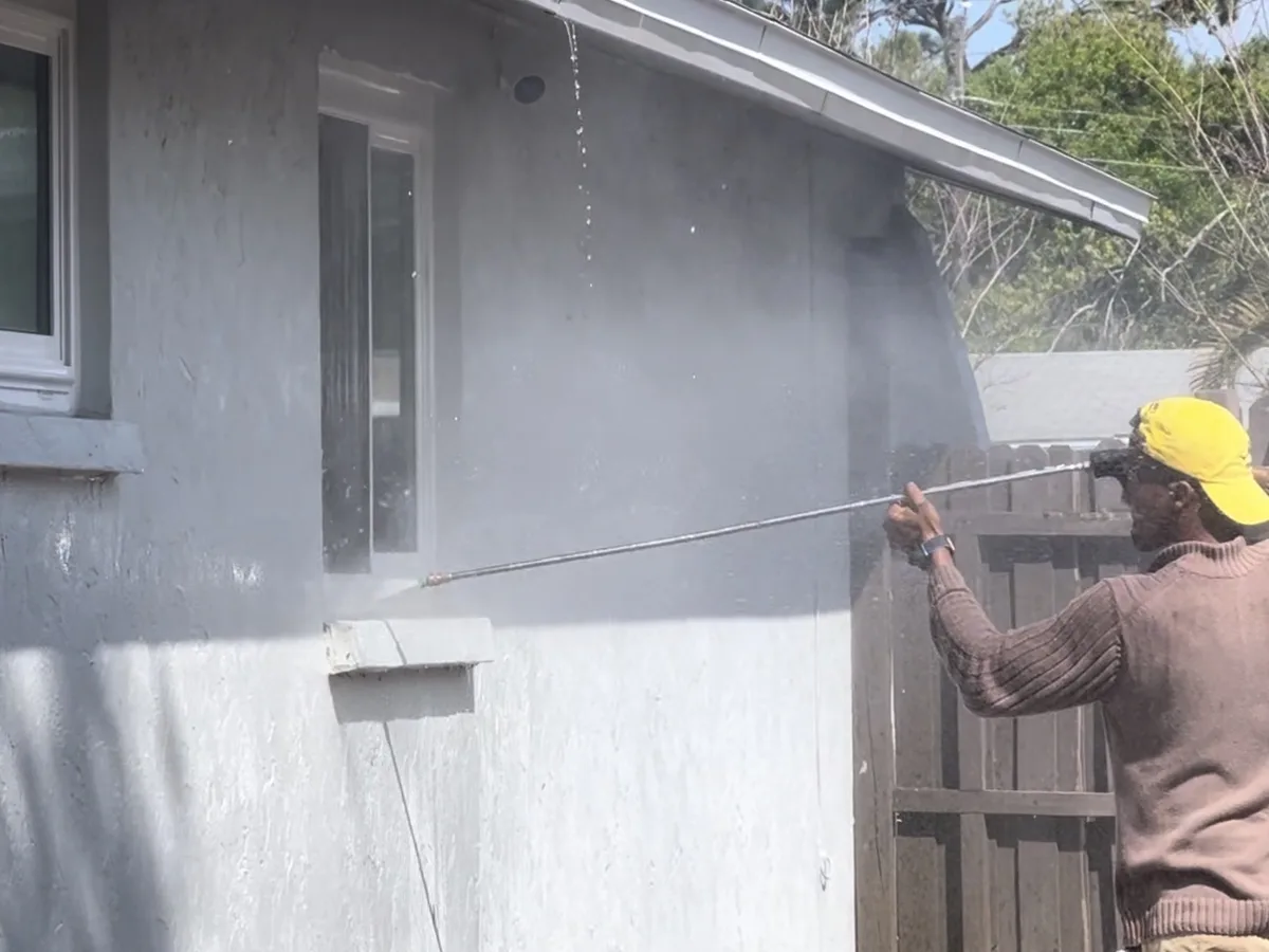 Crew member pressure washing a stucco wall before exterior painting
