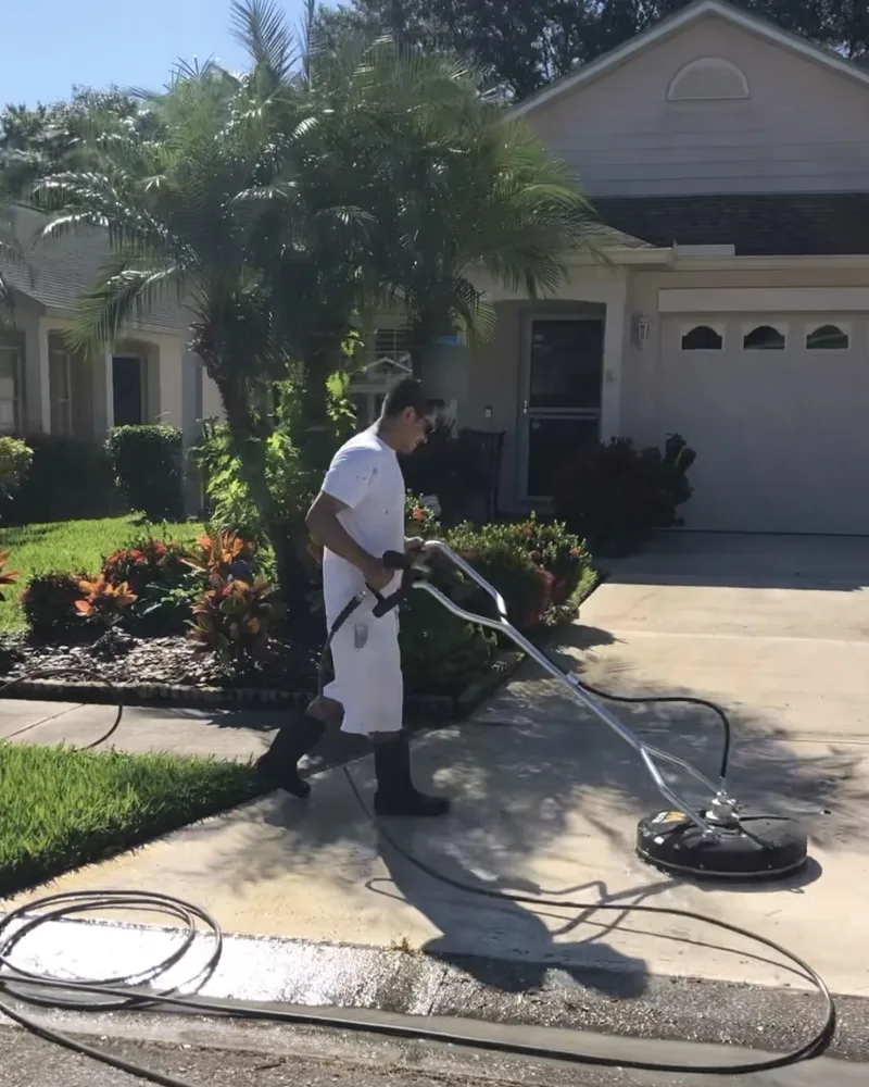 Crew member cleaning a concrete driveway with a surface cleaner