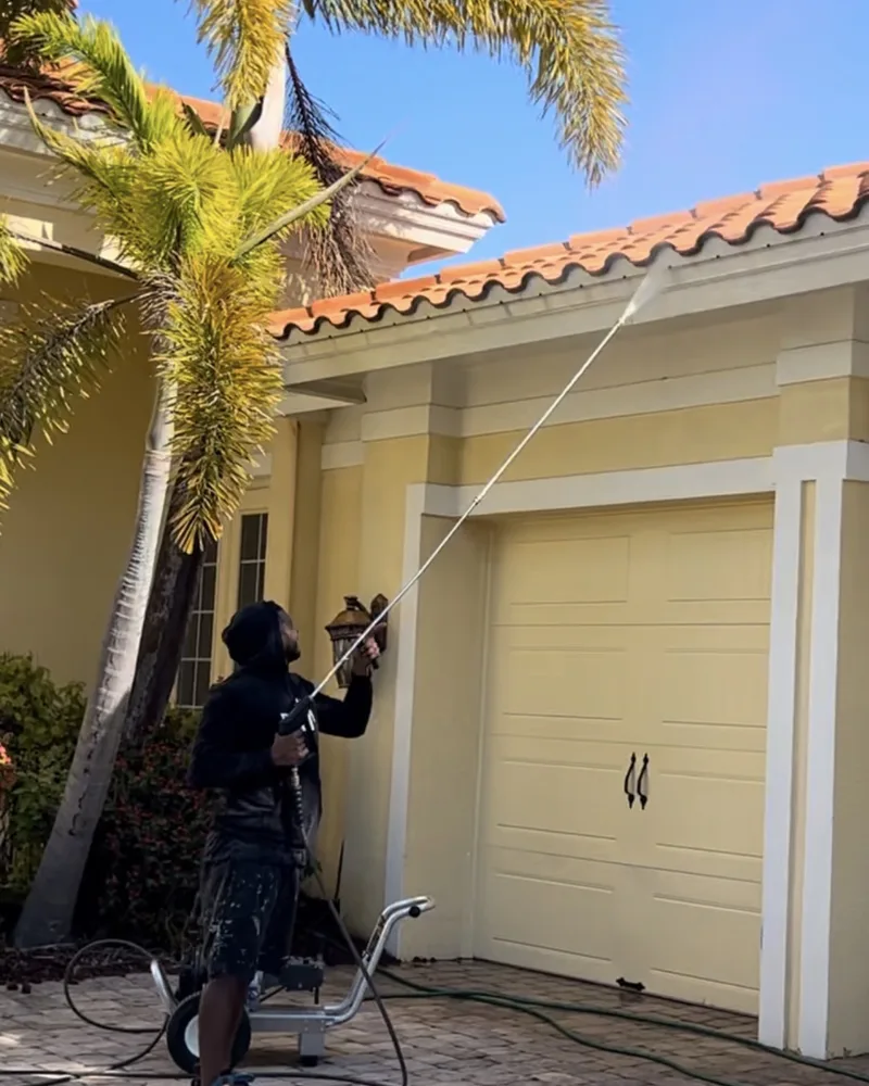 Crew member washing eaves and fascia under a tile roof with an extension wand