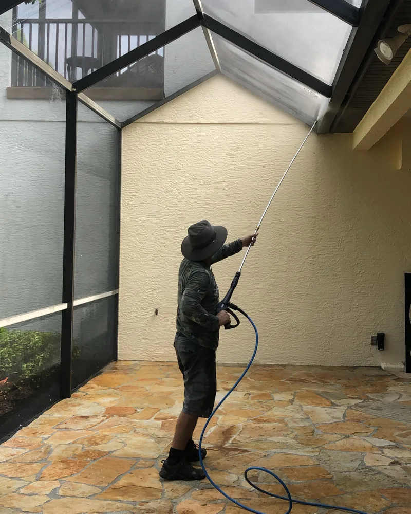 Crew member washing a pool screen enclosure frame on a flagstone lanai