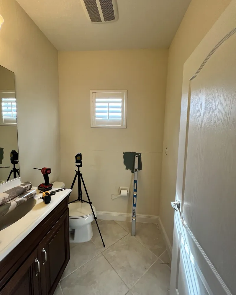Before: plain beige half bath with laser level and tools set up to lay out wainscoting