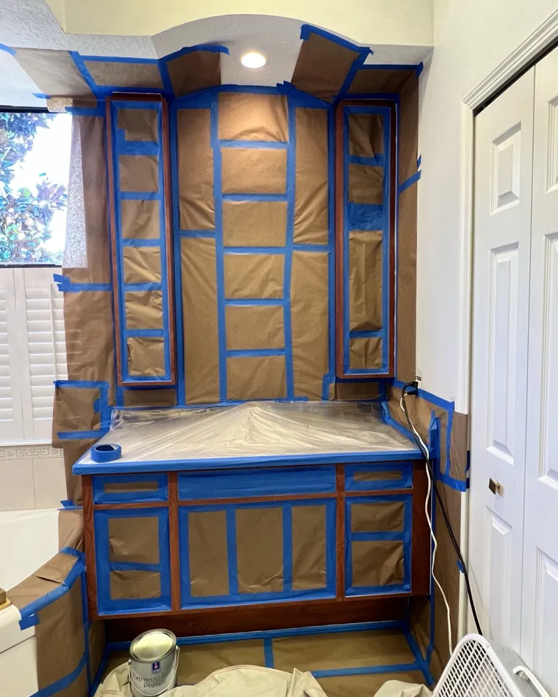 Before: dark wood bathroom vanity and tall cabinets fully masked with paper and tape, Sherwin-Williams Extreme Bond Primer ready