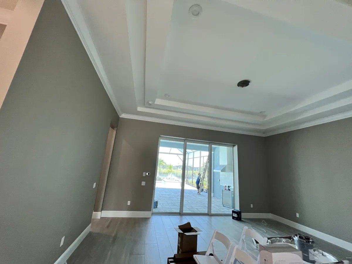 After: living room with finished crown molding on a stepped tray ceiling and sliding doors to the lanai