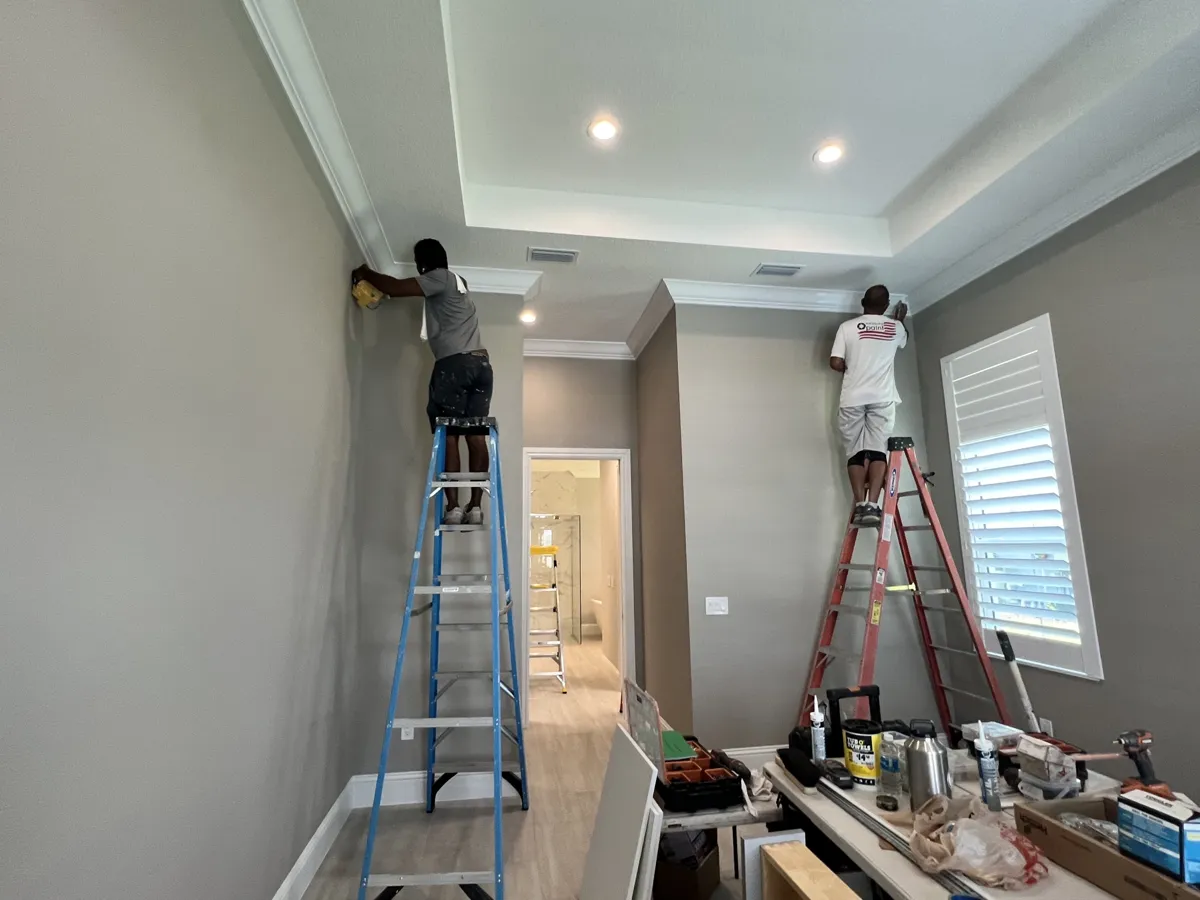 During: two crew members on ladders installing crown molding along a tray ceiling