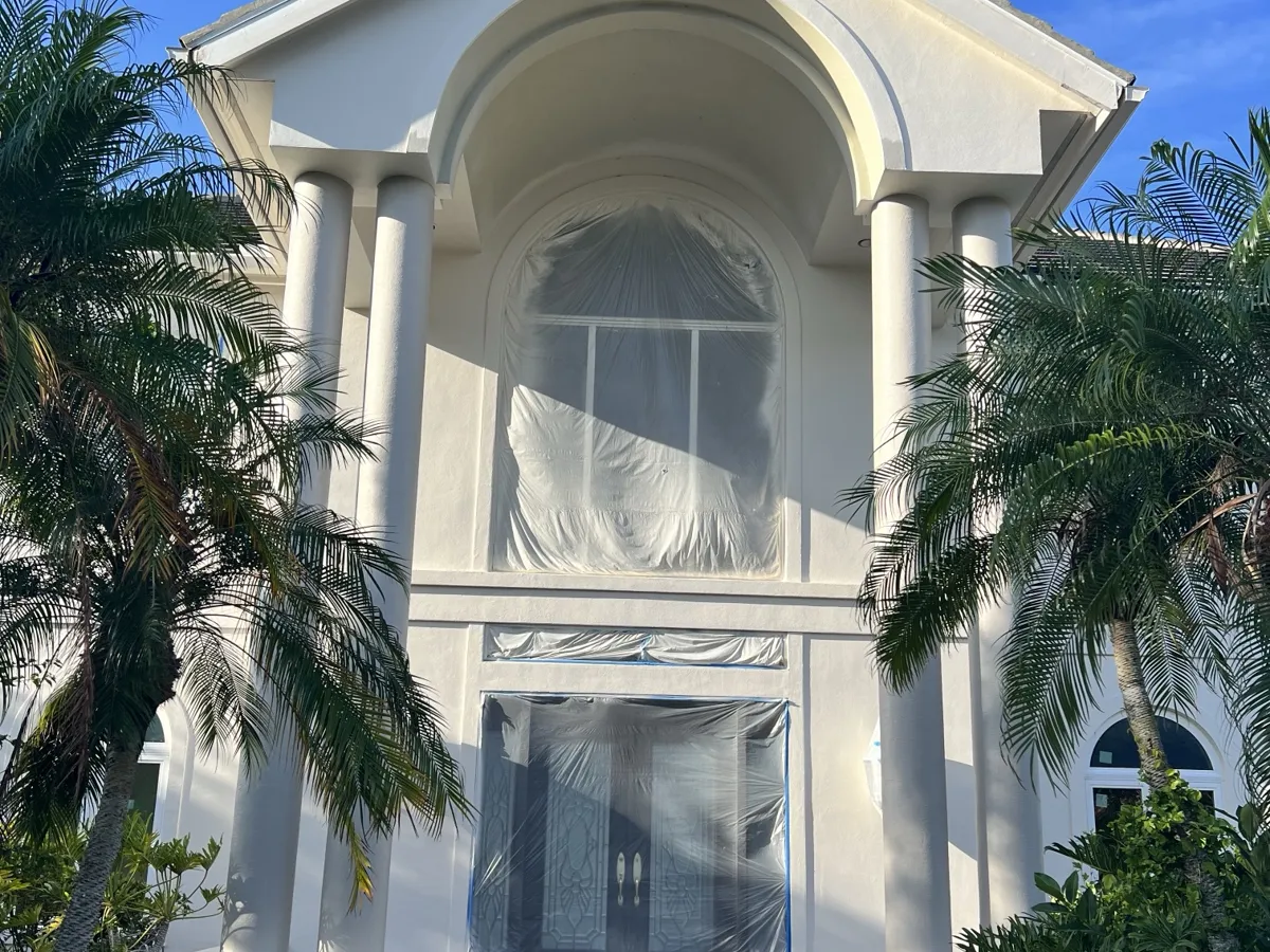 Two-story columned entry with the arched window and front doors masked in plastic for spraying