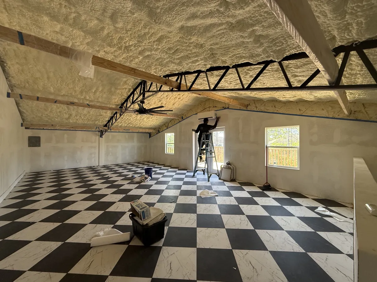 Before: open loft with exposed yellow spray-foam ceiling, steel trusses and checkerboard floor