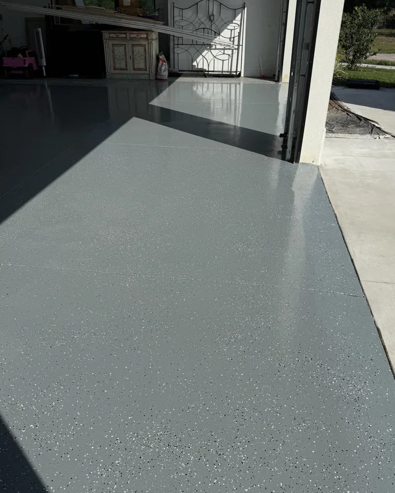 After: the finished garage floor with a glossy gray coating and decorative flakes up to the garage door