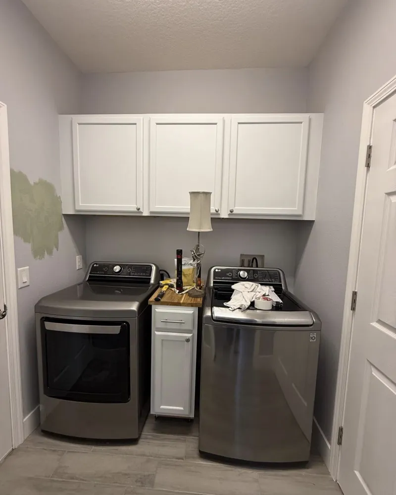 Before: plain laundry room with side-by-side washer and dryer under white upper cabinets