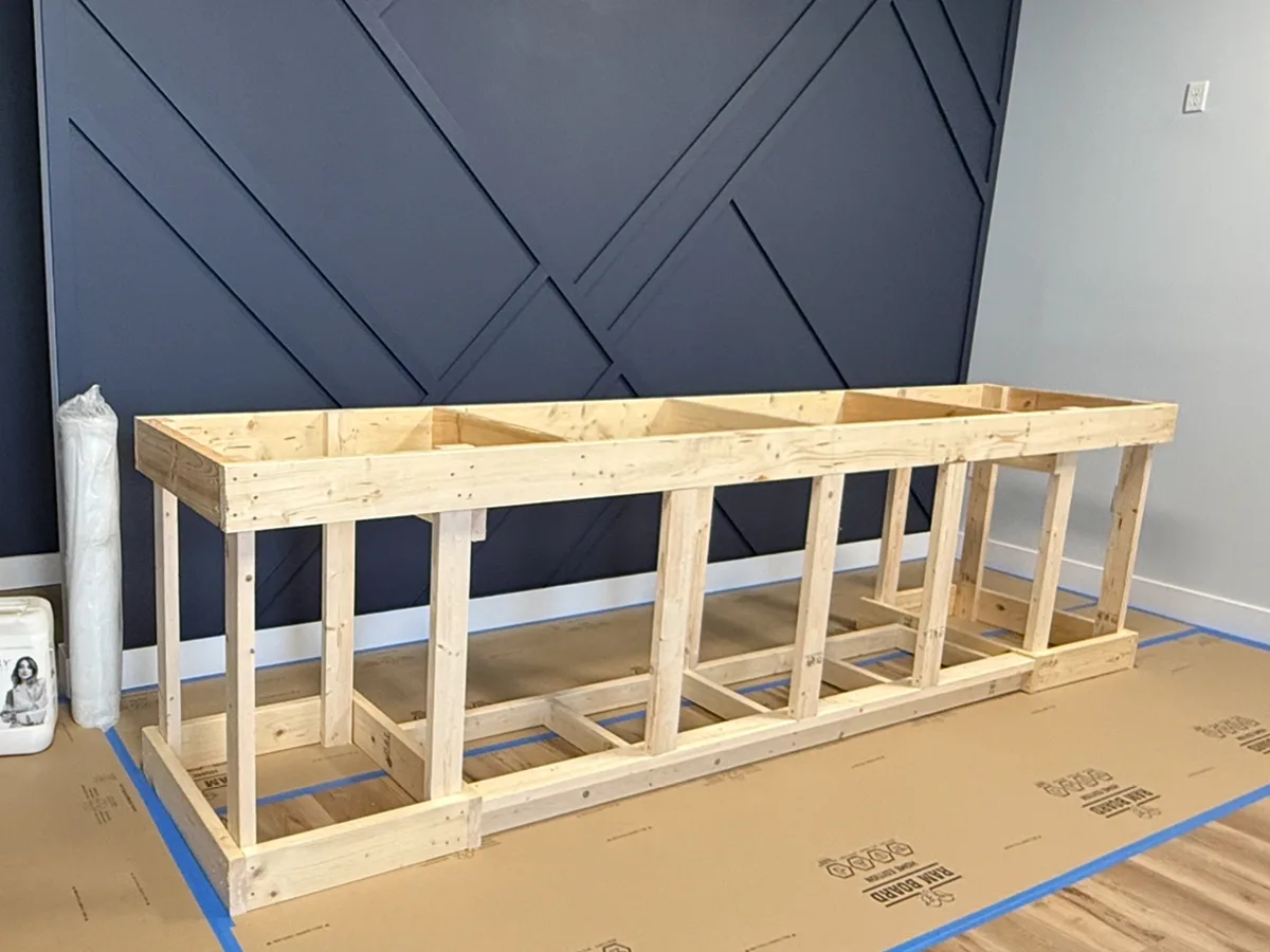 Framing: wood-framed reception desk in front of a navy geometric accent wall, floor protected with Ram Board