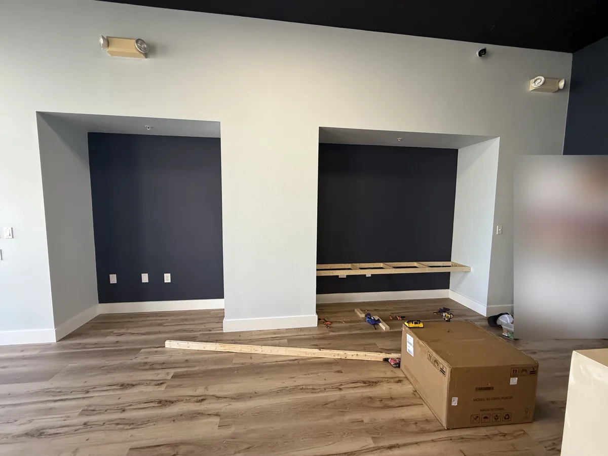 Before: two empty wall niches with navy back walls, first shelf frame being installed