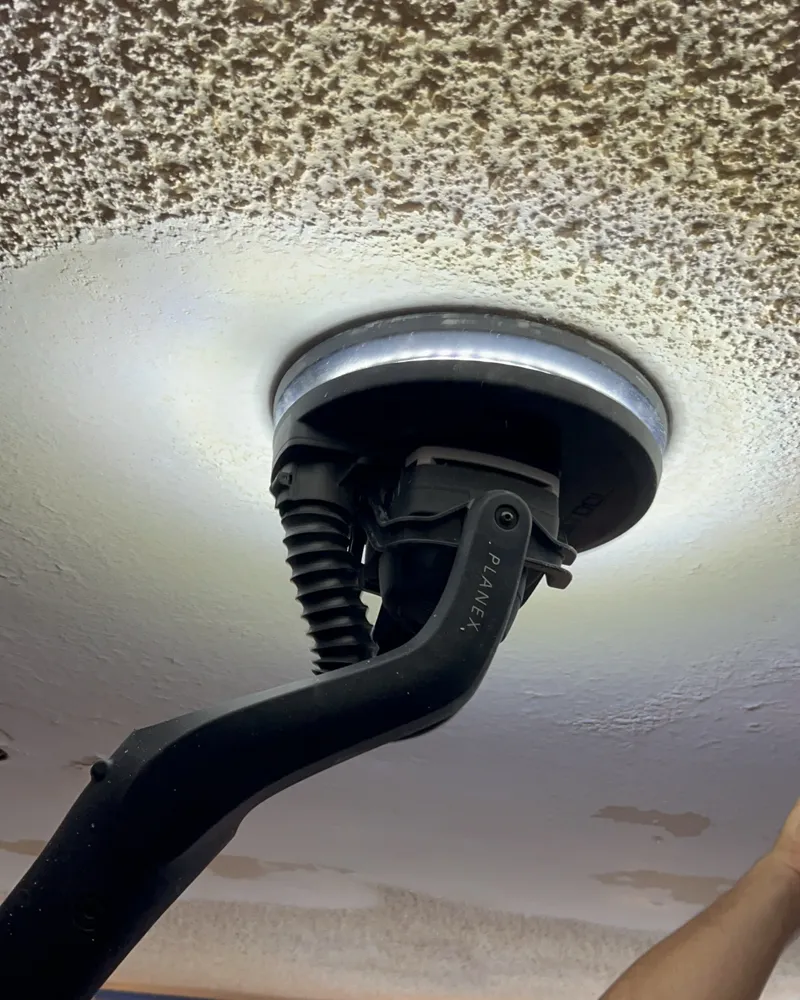 Close-up: the long-reach sander leaving a smooth band through the popcorn texture