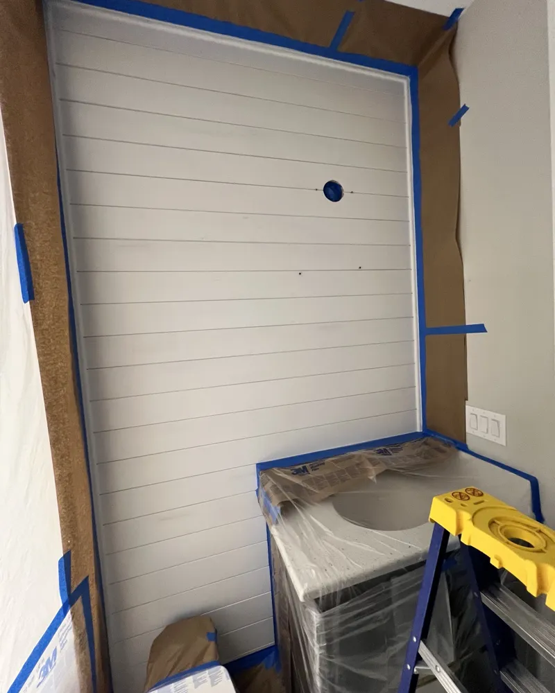 During: new shiplap wall in a half bath, primed, with vanity and toilet wrapped and walls masked