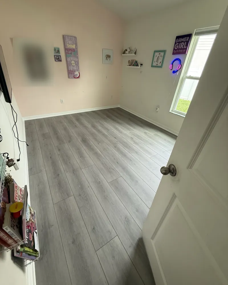 After: the same bedroom with gray wood-look luxury vinyl plank flooring and white baseboards