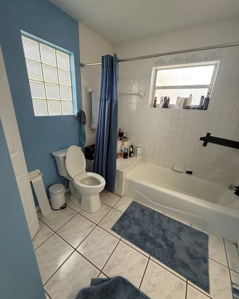 Before: dated bathroom with a tub, shower curtain and small white wall tile