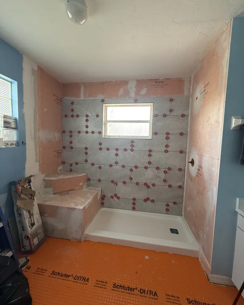 During: tub removed, shower pan set, Schluter-KERDI waterproofing on walls and bench, DITRA on the floor, large-format tile going up with leveling clips