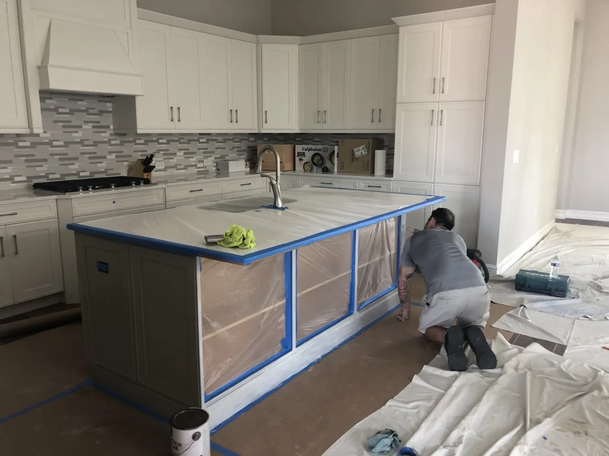 Before: kitchen island in a gray finish being prepped, counters and floor protected