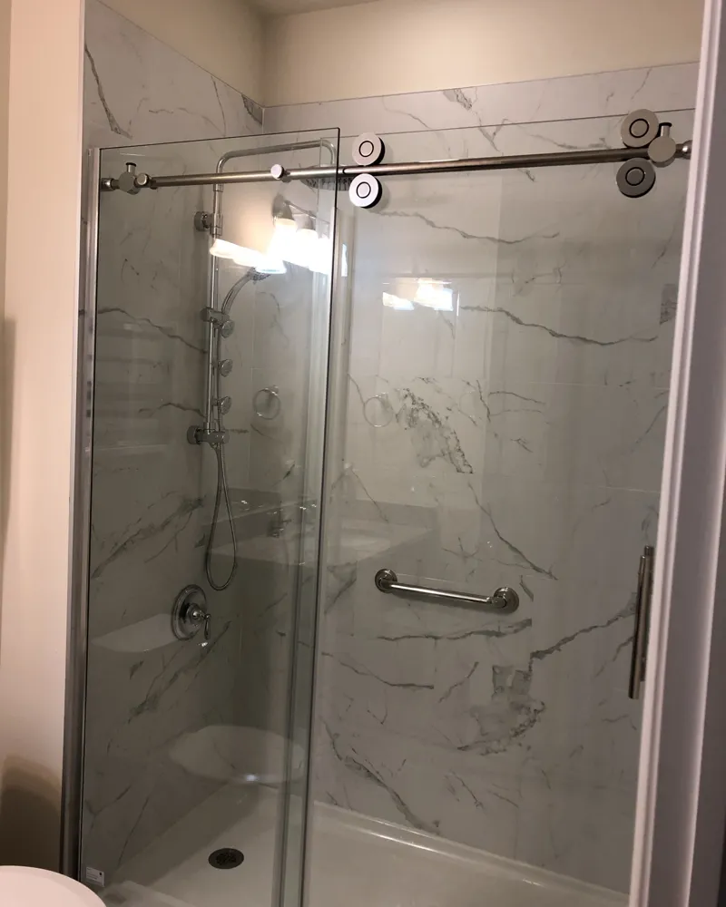 After: new shower with large marble-look porcelain walls, sliding glass barn-style door, shower panel and grab bar