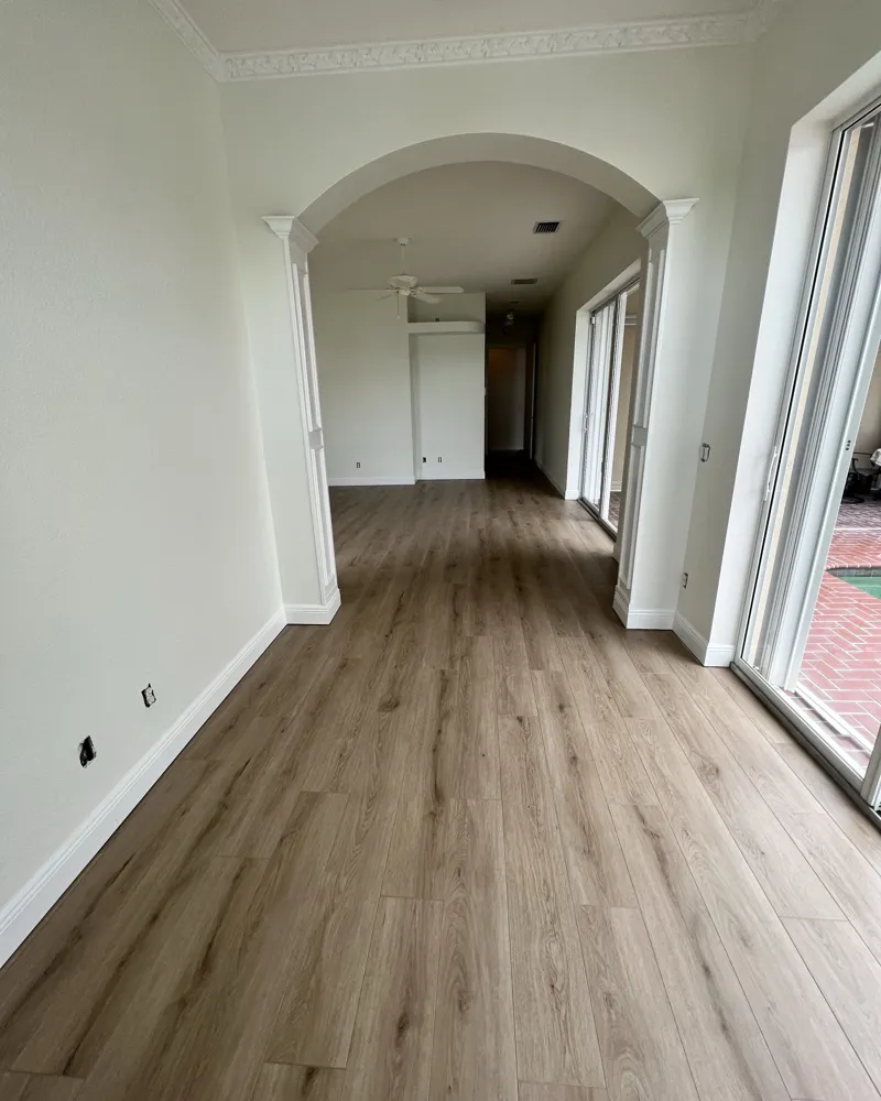 After: light oak luxury vinyl plank flowing through the living area and archway, with fresh paint and white baseboards
