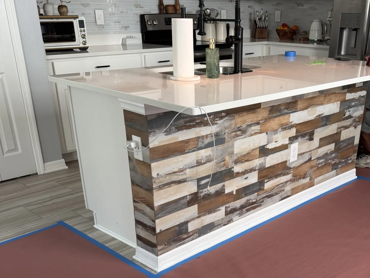 Before: kitchen island side covered in rustic multicolor wood-look planks with white base trim