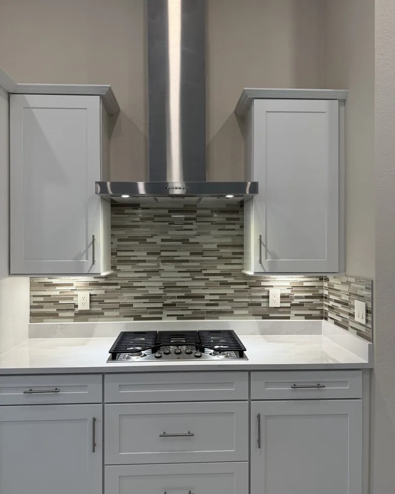 After: linear glass mosaic tile backsplash under the range hood and along the countertop, with outlets and switch reset