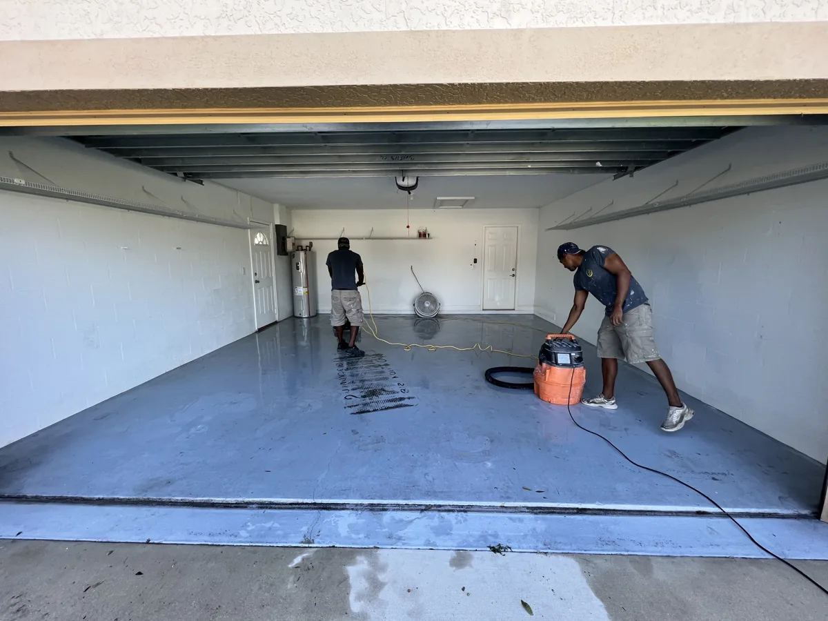 Process: crew machine-scrubbing and vacuuming the worn blue-gray garage floor coating before recoating
