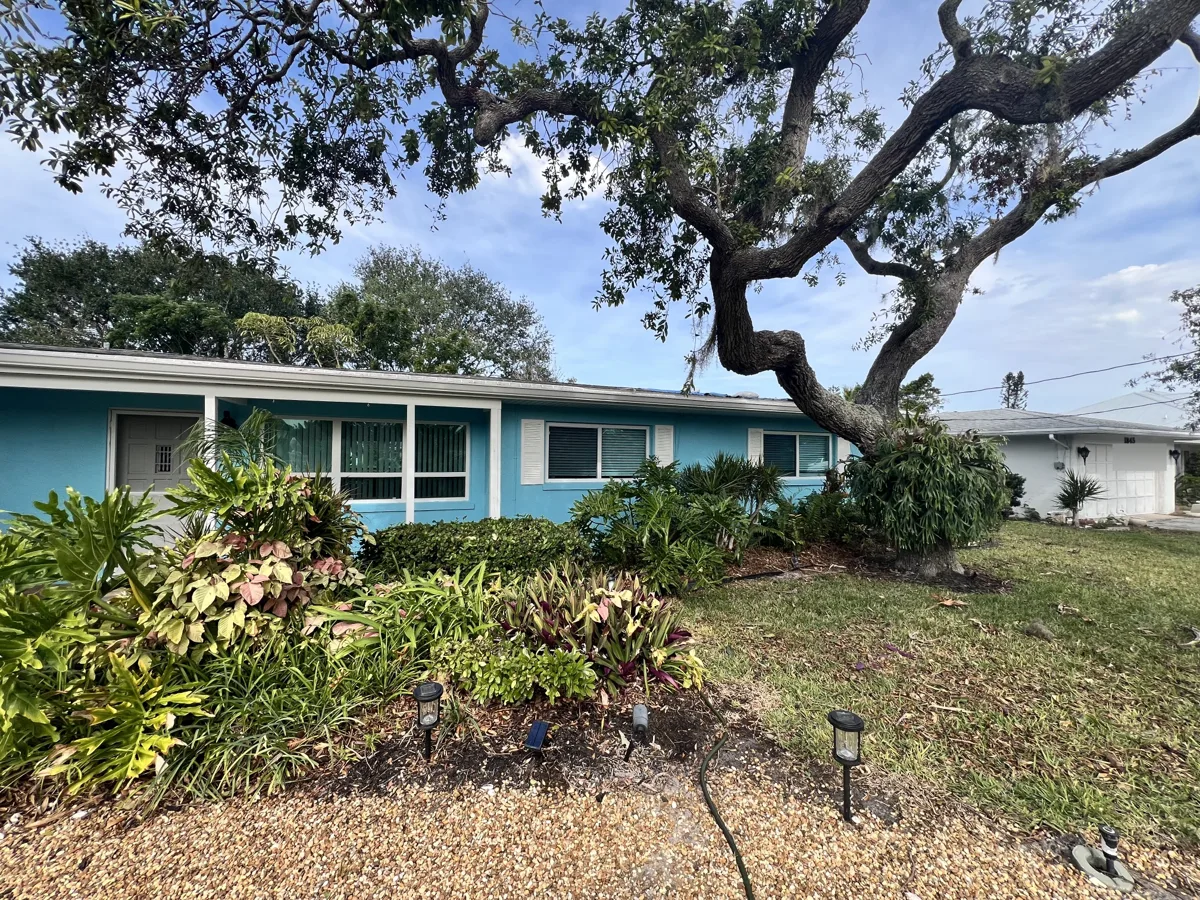 After: the same home repainted in a bright coastal turquoise with crisp white trim, shutters and fascia