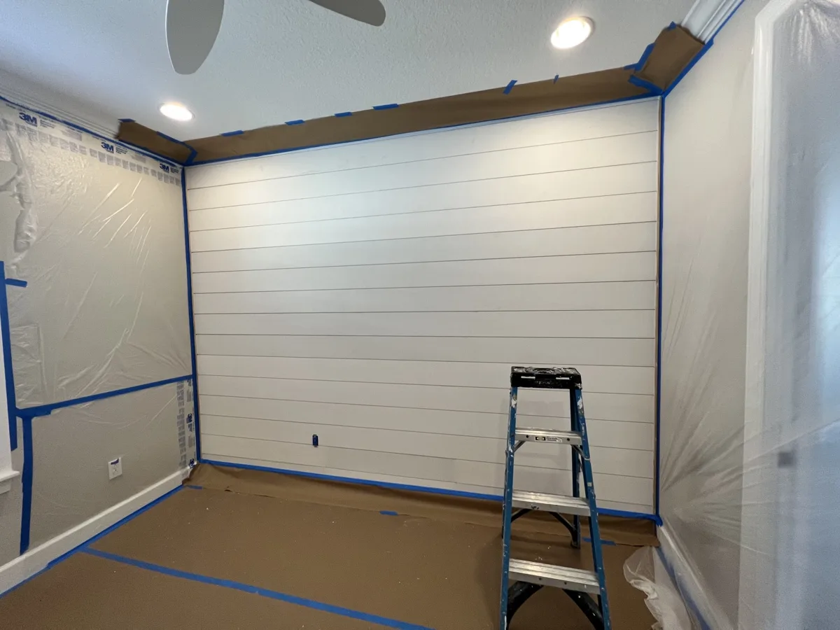 Process: new shiplap accent wall installed and primed white, with the room fully masked and floors protected
