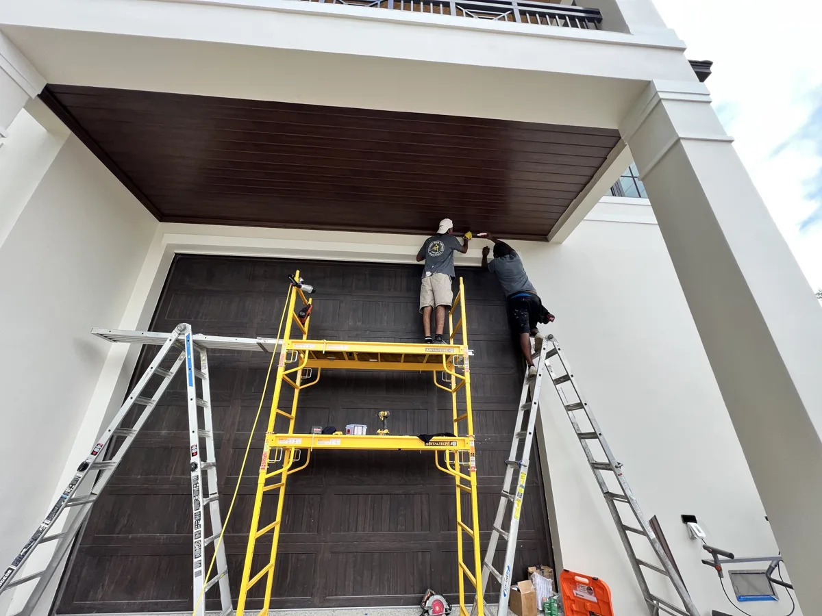 Process: Florida Doug Services crew on scaffolding installing wood-grain PVC ceiling trim above the garage
