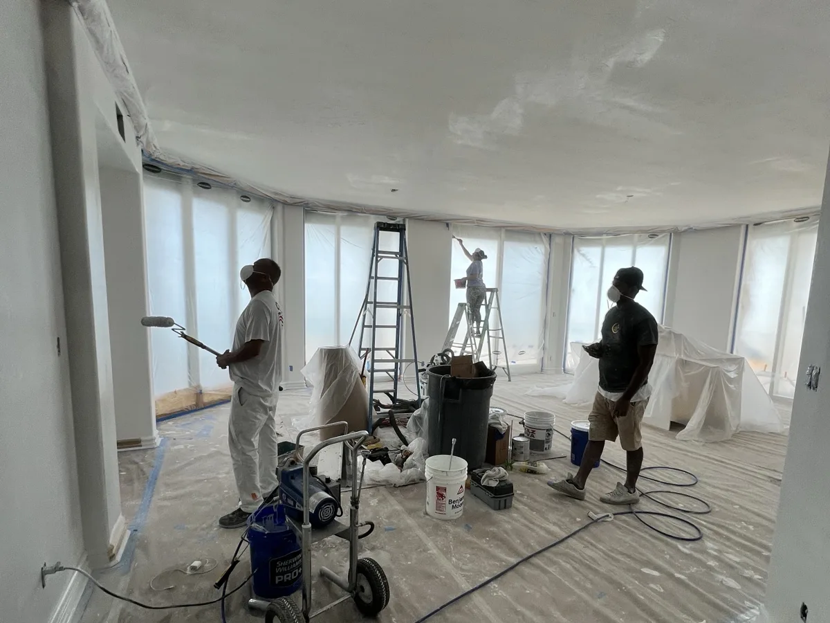 Process: crew finishing walls and ceilings with the Graco sprayer, windows and floors fully masked