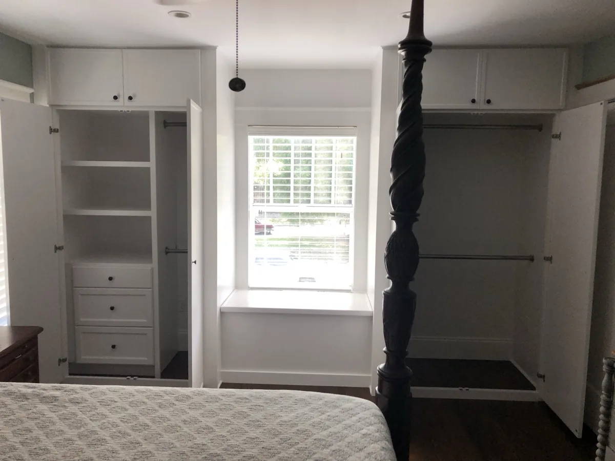 After: painted white built-in closets open, showing shelves, drawers and double hanging rods on both sides of the window seat