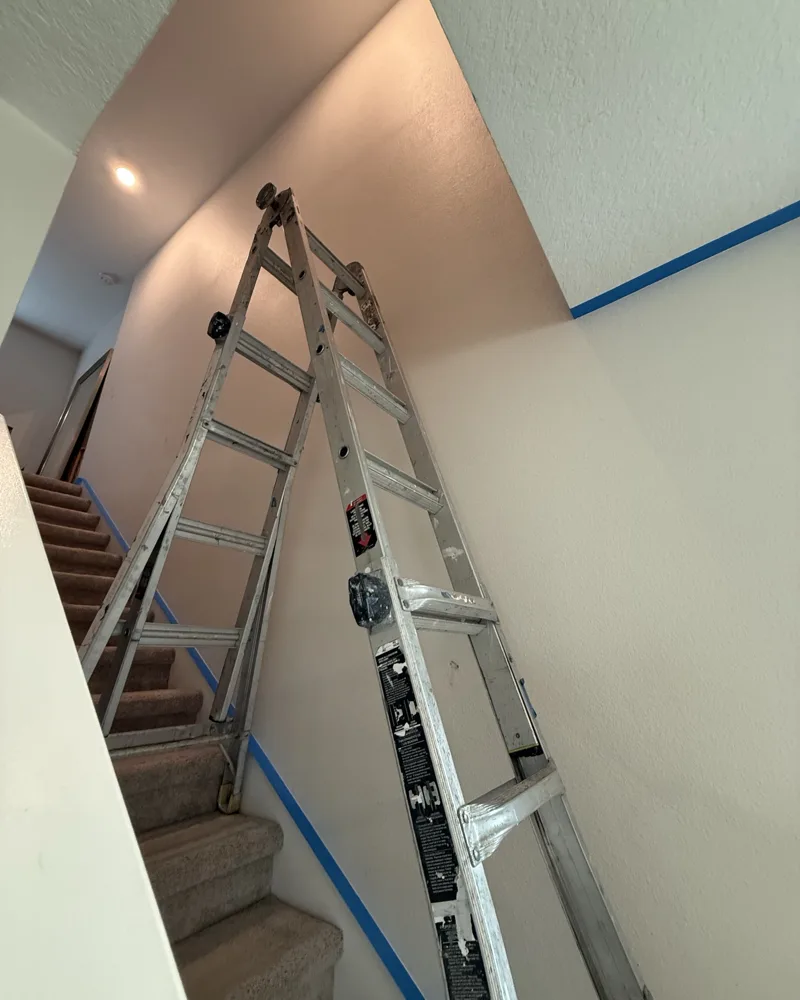Before: tall two-story stairwell wall taped off with a ladder set on the stairs