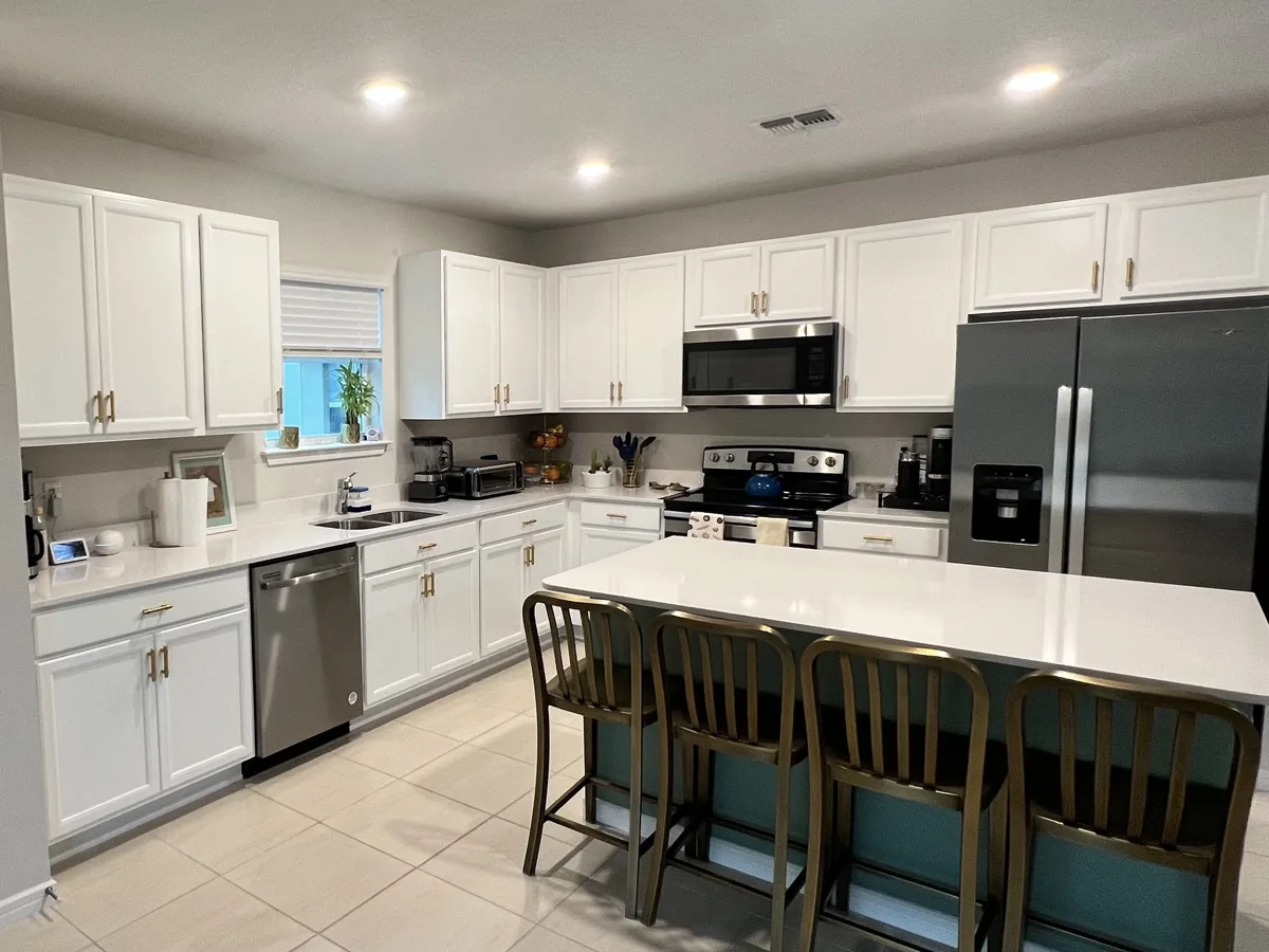 Dark kitchen cabinets painted bright white with a teal island and gold hardware in Parrish