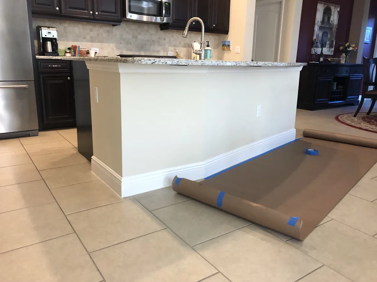Before: plain painted drywall kitchen island with white baseboard under a granite countertop