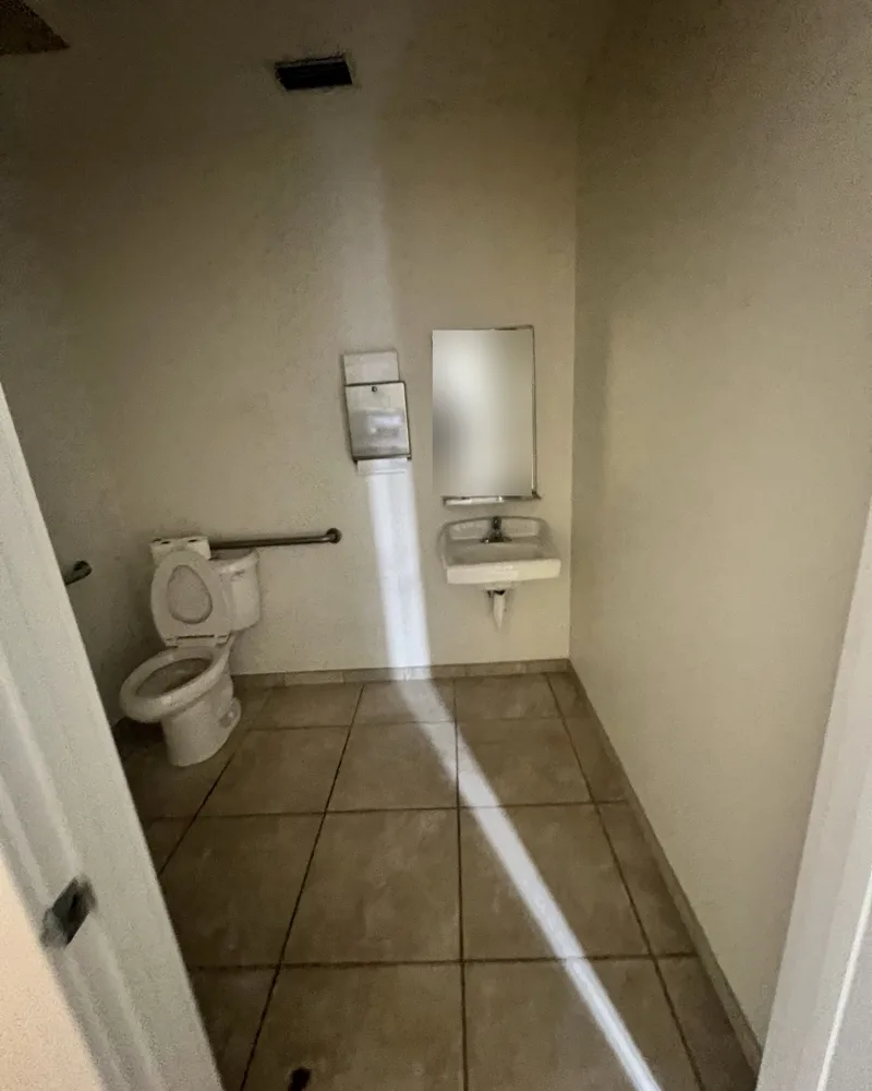 Before: dated commercial restroom with beige tile floor, plain walls and a small wall-hung sink